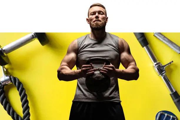 A gym member holding a kettlebell, with a barbell, battle rope and weights around them